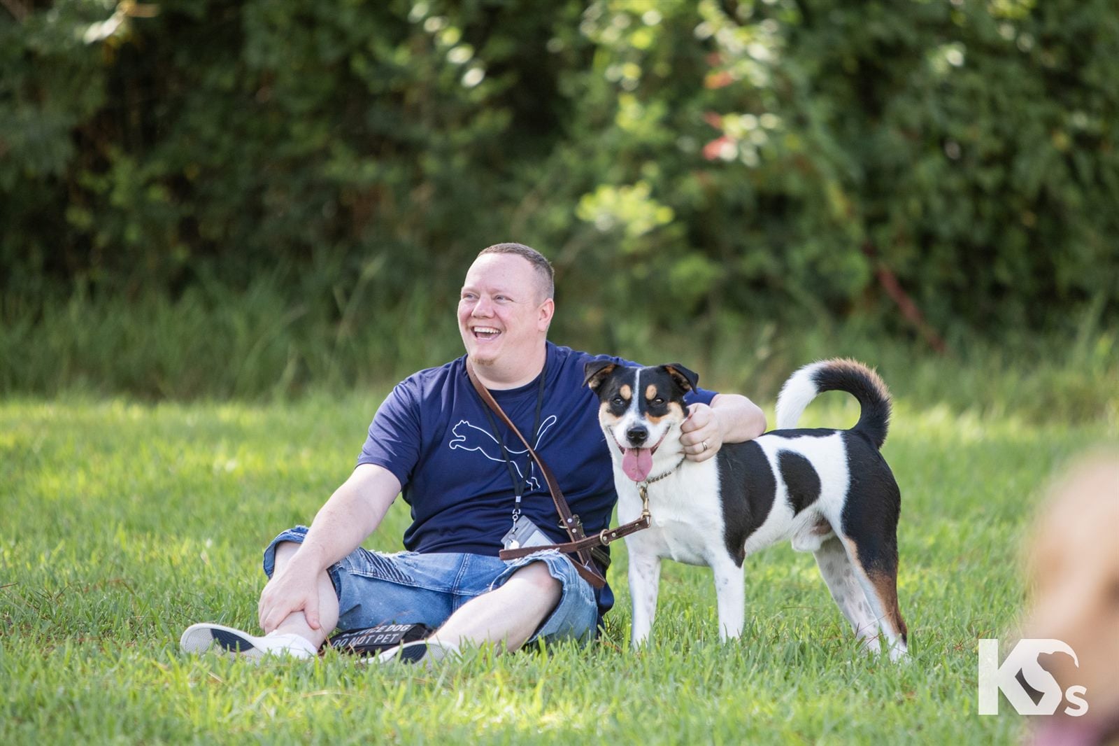 A Veteran sitting in the grass beside his black and white Service Dog.