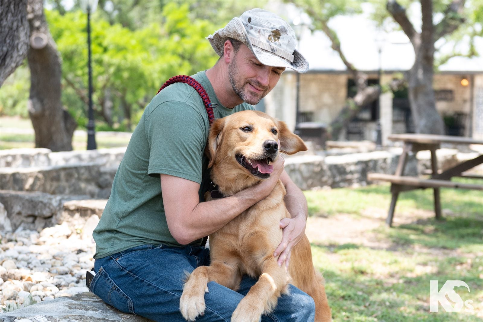 A Veteran kneeling in a park with his golden Service Dog held close.