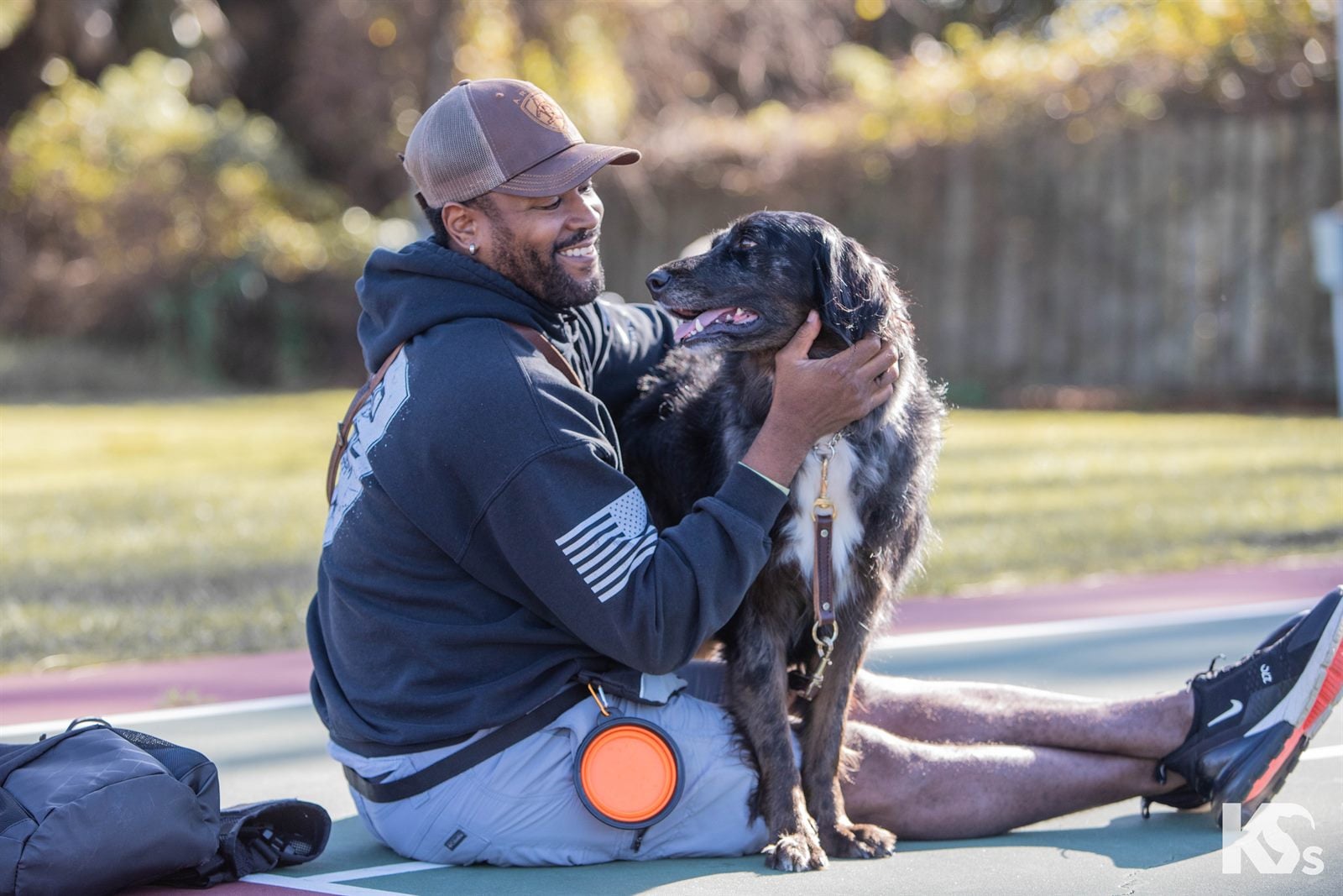 A Veteran kneeling on the grass, holding his Service Dog's face in both hands.